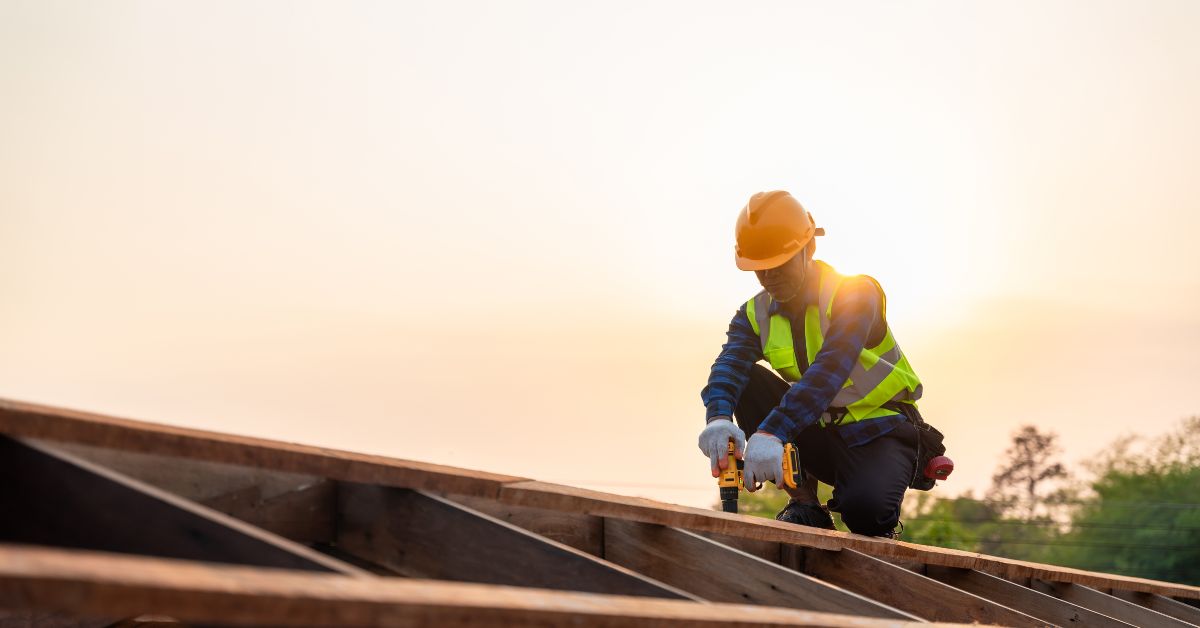 roofing professional installing new roof construction, kneeling on roof using nail gun