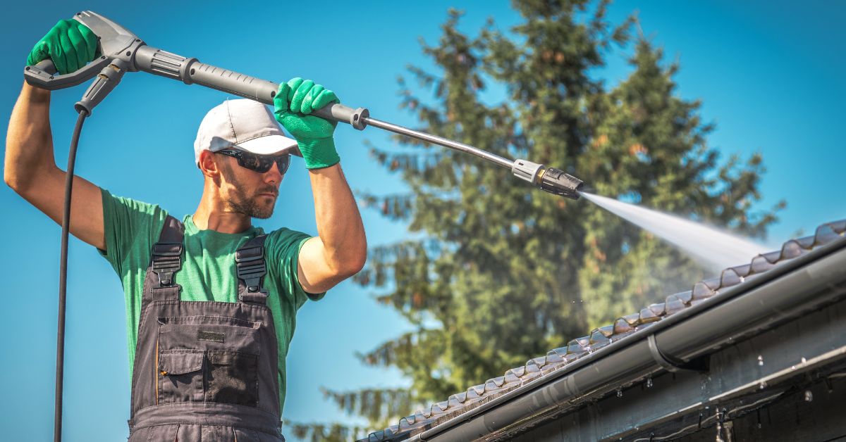 roof worker pressure washing a metal roof