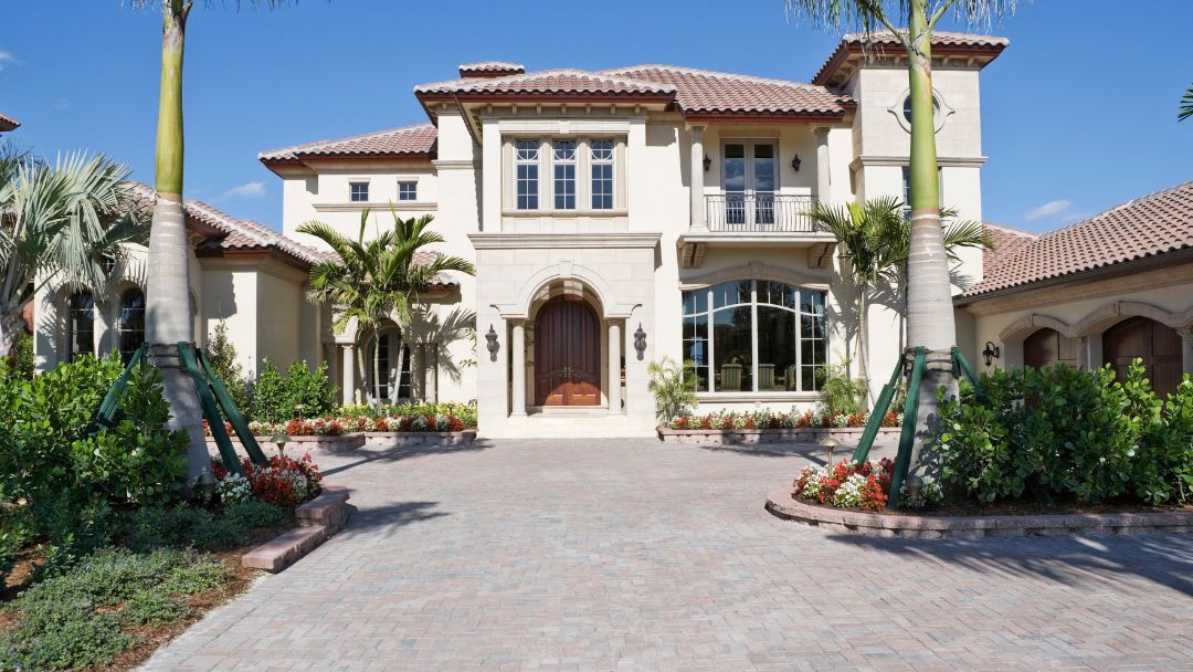 Front view of mansion with tile roof with driveway and palm trees