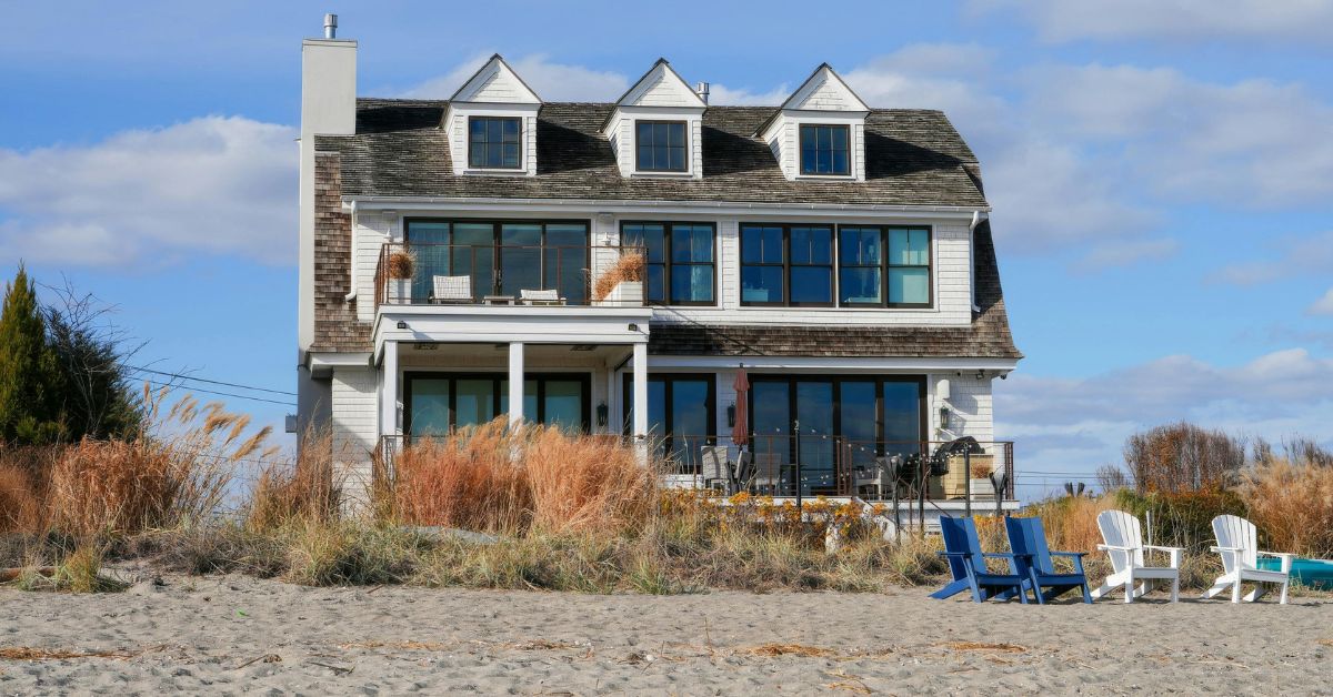 2-story white beach house with sand and grasses